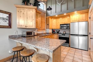 A kitchen with wooden cabinets, a granite countertop, a stainless steel refrigerator, a microwave, a toaster, and a kettle.