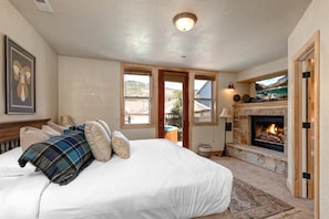 A bedroom with a bed, a fireplace, and a view of the outdoors.