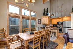 Une cuisine spacieuse avec des meubles en bois, un coin repas comprenant une table et des chaises en bois, et une grande fenêtre avec des stores.