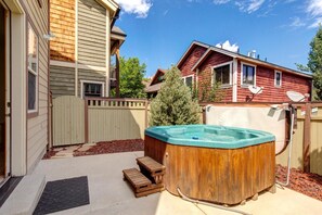 A backyard with a wooden hot tub, a wooden deck, and a red house.