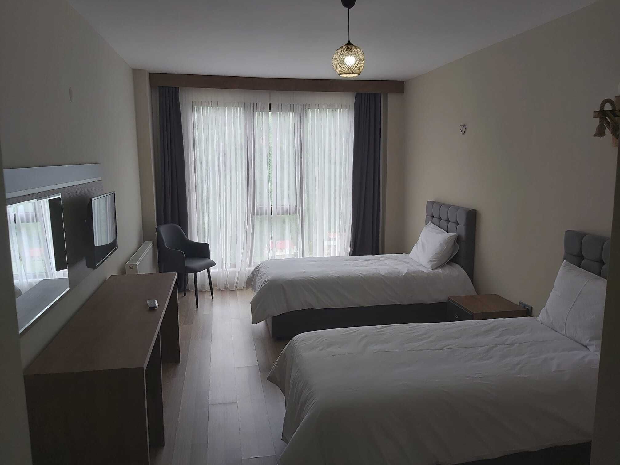 A hotel room with two beds, a desk with a TV, a chair, and a large window with sheer curtains.