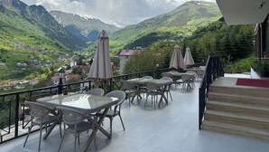 Une terrasse agrémentée de tables et de chaises, offrant une vue sur un paysage montagneux avec un village en contrebas.