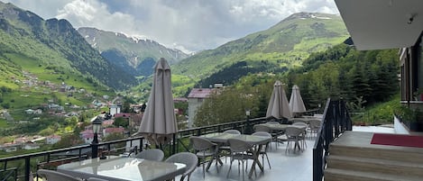 Una terraza con mesas y sillas, con vistas a un paisaje montañoso y un pueblo abajo.