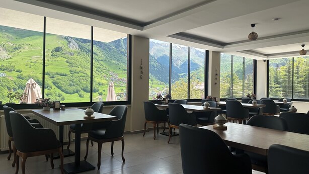 Un espace repas avec des tables et des chaises, de grandes fenêtres offrant une vue sur les montagnes et des luminaires au plafond.
