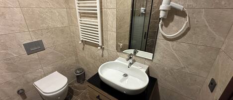 A bathroom with a white toilet, a sink with a mirror, a towel rack, and a hairdryer.