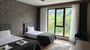 Ein Hotelzimmer mit zwei Betten, einem großen Fenster mit Blick auf Grünflächen, einem dunkel gefärbten Stuhl und einem gemusterten Teppich.