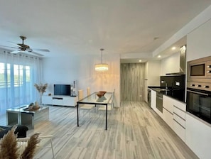 A modern kitchen with a built-in oven, microwave, and stove. There is a dining area with a glass table and chairs. - Beautiful new apartment in Tarifa with views to the Strait of Gibraltar, very good location. (Tarifa)