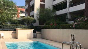 Une piscine avec un escalier en métal, entourée d’un petit muret et de verdure.