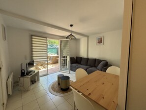 A living room with a wooden dining table, a sofa, and a TV. - Apt In The City Center/ Residence With Pool (Saint-Raphaël)