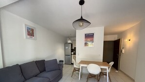 Un salon moderne avec un canapé gris, une table à manger avec des chaises, un coin cuisine et un réfrigérateur.