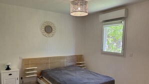 Une chambre à coucher comprenant un lit, une table de chevet, un miroir fixé au mur, une fenêtre donnant sur un espace verdoyant et un luminaire au plafond.