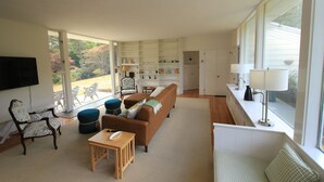 A spacious living room with a large window, a sofa, a coffee table, and a bookshelf. - 86 Spring Hill - Private Pool (Sandwich)
