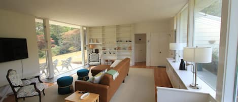 A spacious living room with a large window, a sofa, a coffee table, and a bookshelf.