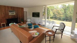 Una sala de estar moderna con un sofá marrón, otomanas azul verdoso y un televisor en la pared.