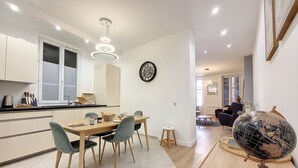 A modern kitchen with a dining area, featuring a wooden table, chairs, and a globe on a side table. - N&J - LE PIERLAS - Place Garibaldi - Very close Old Town (Niza)