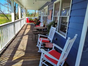Relax on the covered porch with a comfortable seating area, featuring white rocking chairs and a small table.