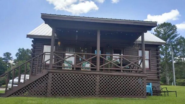 A wooden cabin with a covered porch, a staircase leading up to the entrance, and a fenced area with a bench. - Sweet Serenity where peace is a necessity! (Franklin)