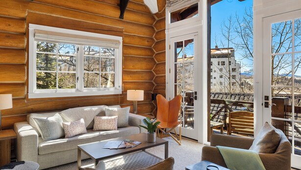 L’intérieur d’une cabane en rondins, avec un canapé, un fauteuil, une table basse et une vue sur l’extérieur à travers une porte vitrée.