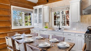 L’intérieur d’une cabane en rondins comprend un coin repas, des meubles blancs et une cuisine équipée d’une cuisinière.