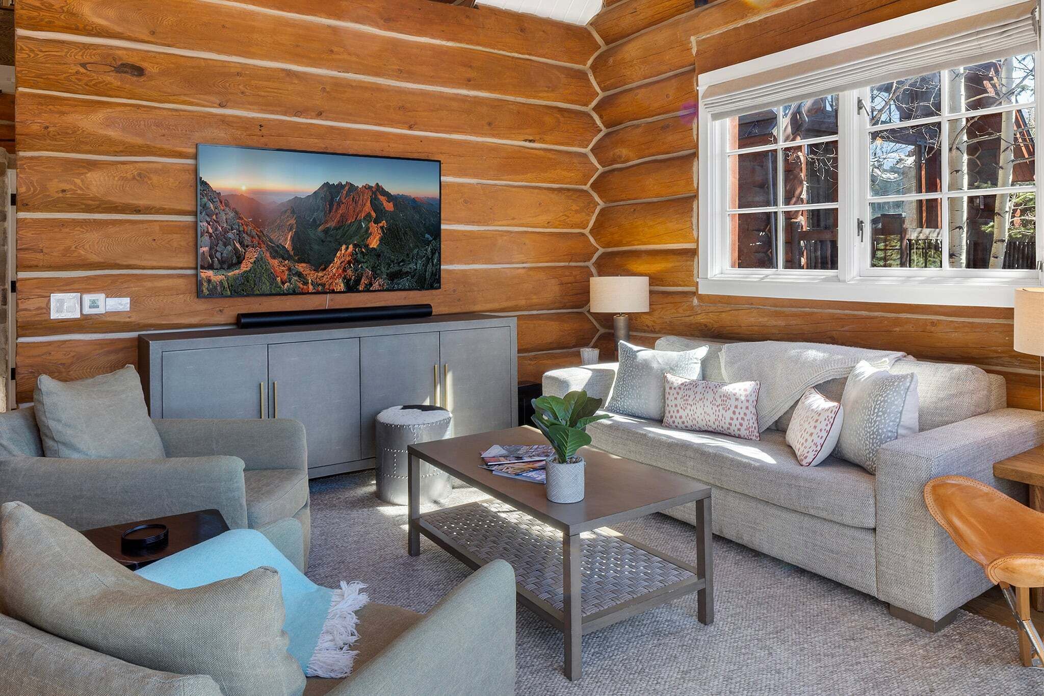 A log cabin interior with a sofa, coffee table, and a television mounted on a wooden wall.