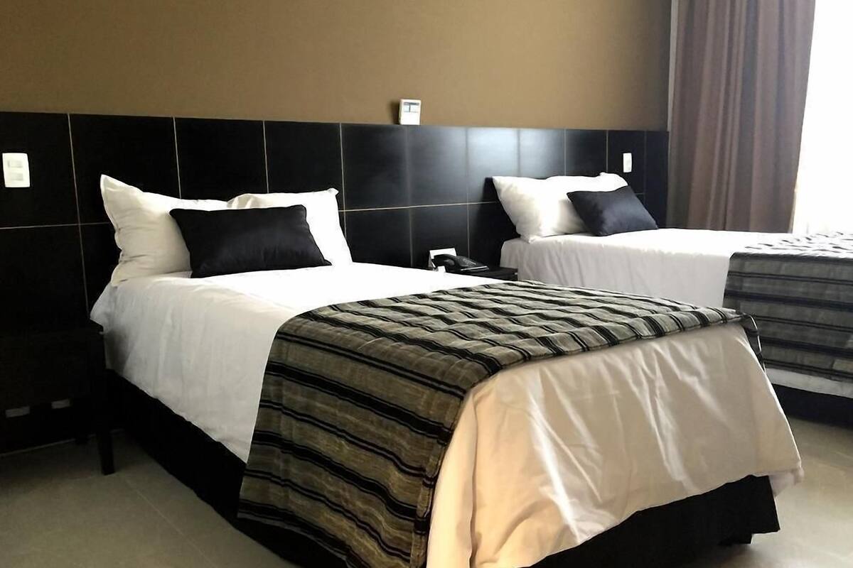Een hotelkamer met twee bedden, elk voorzien van witte lakens en zwarte kussens. De kamer heeft een modern design met een zwart hoofdbord en een groot raam met gordijnen.