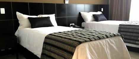 A hotel room with two beds, each with white linens and black pillows. The room has a modern design with a black headboard and a large window with curtains.