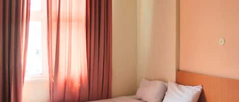 A hotel room with two single beds, a wooden nightstand with a telephone, and a window with curtains.