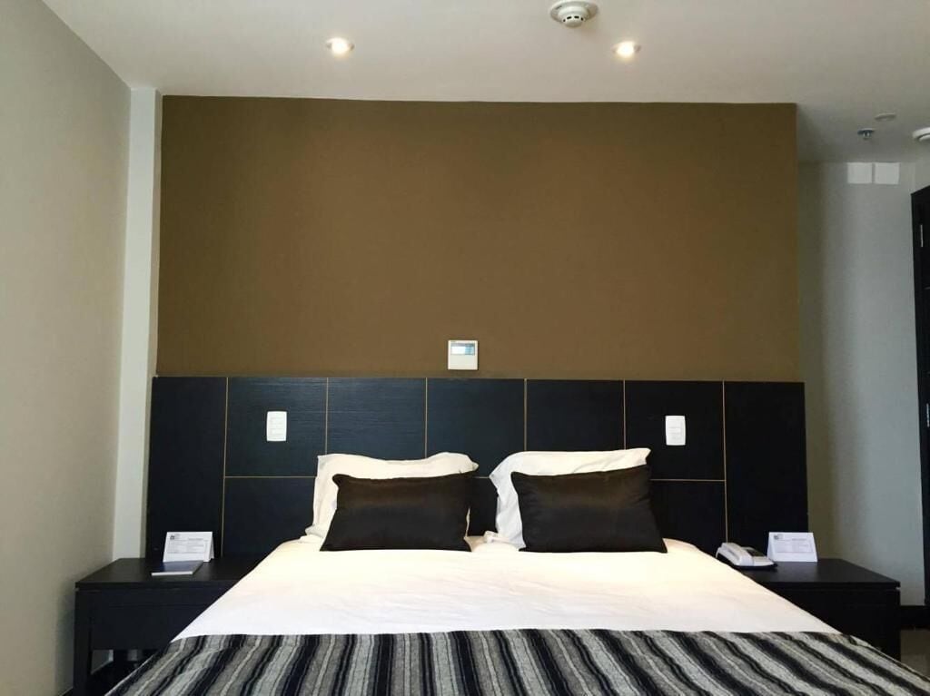 Une chambre d’hôtel avec un grand lit, deux tables de chevet, une tête de lit et un luminaire fixé au mur.