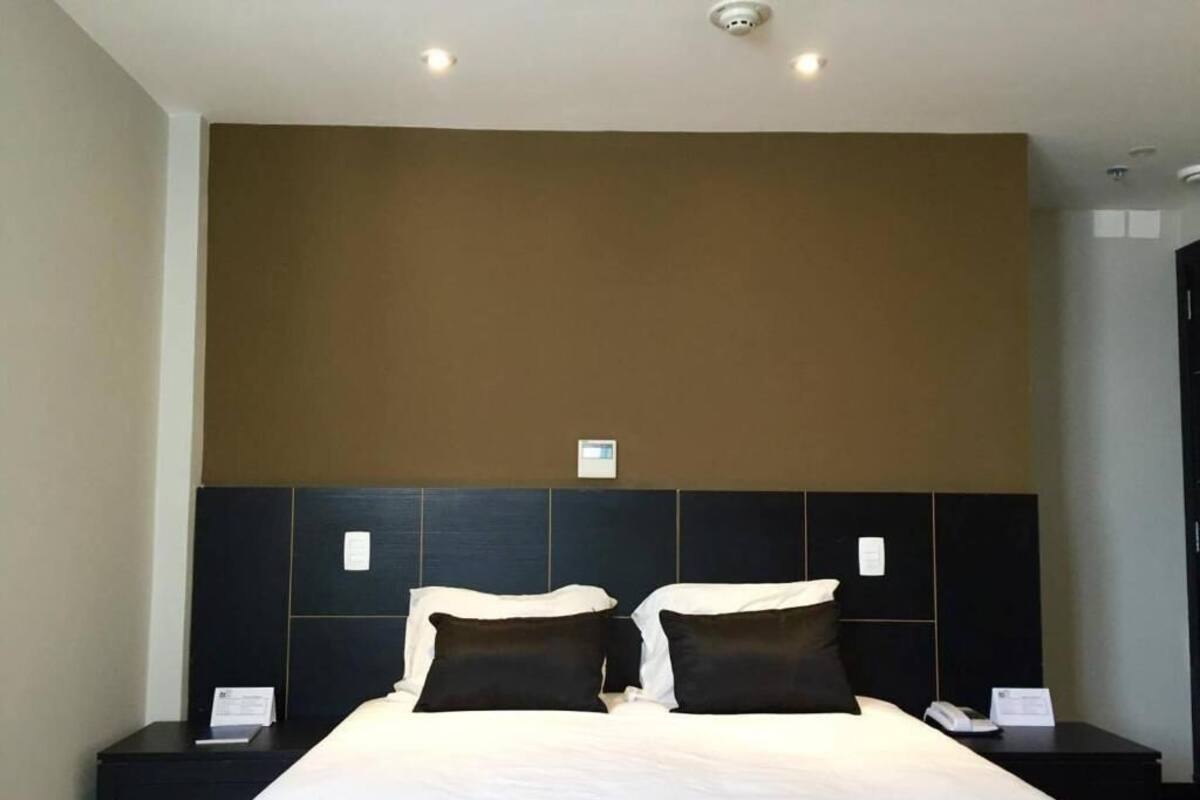 Een hotelkamer met een groot bed, twee nachtkastjes, een hoofdeinde en een wandlamp.