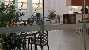 A modern indoor space with glass walls, potted plants, and seating areas. - Hotel Atlântico Tower - SOFT OPENING (Rio de Janeiro)