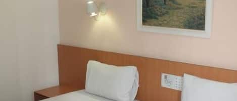 Una camera d'albergo con due letti singoli, una testiera in legno, una lampada a parete e un quadro con un paesaggio.