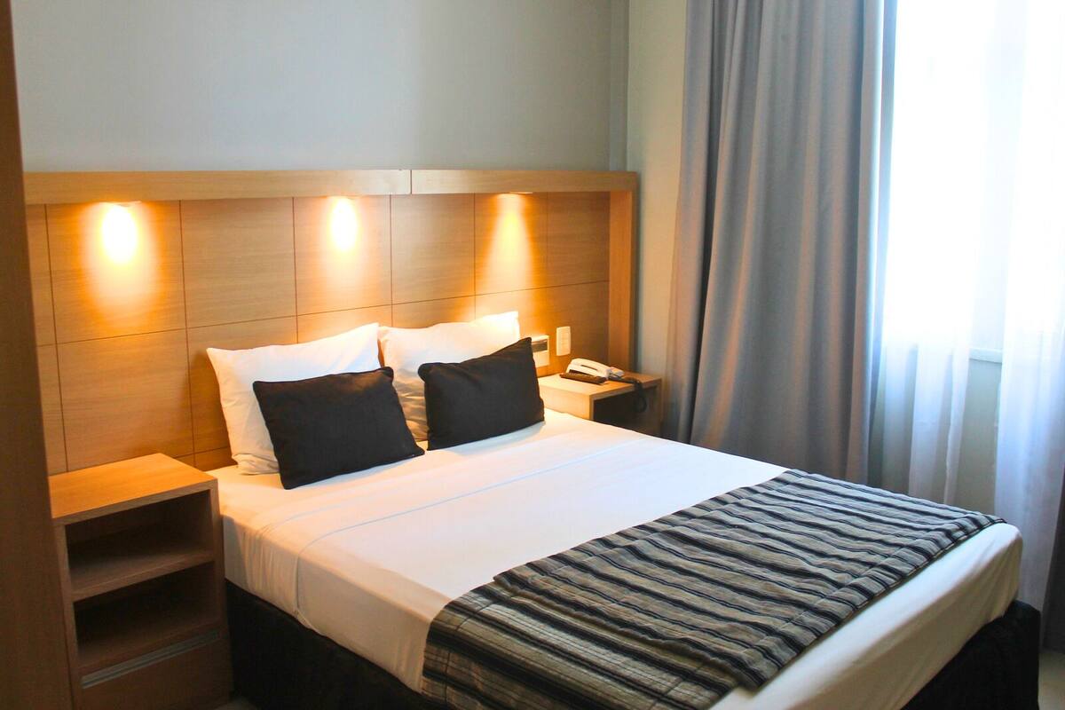 Een hotelkamer met een keurig opgemaakt bed, een nachtkastje met een telefoon en een hoofdbord met ingebouwde verlichting.