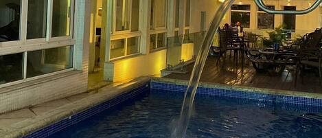 A swimming pool with a waterfall feature, surrounded by a building with large windows and a modern architectural design.