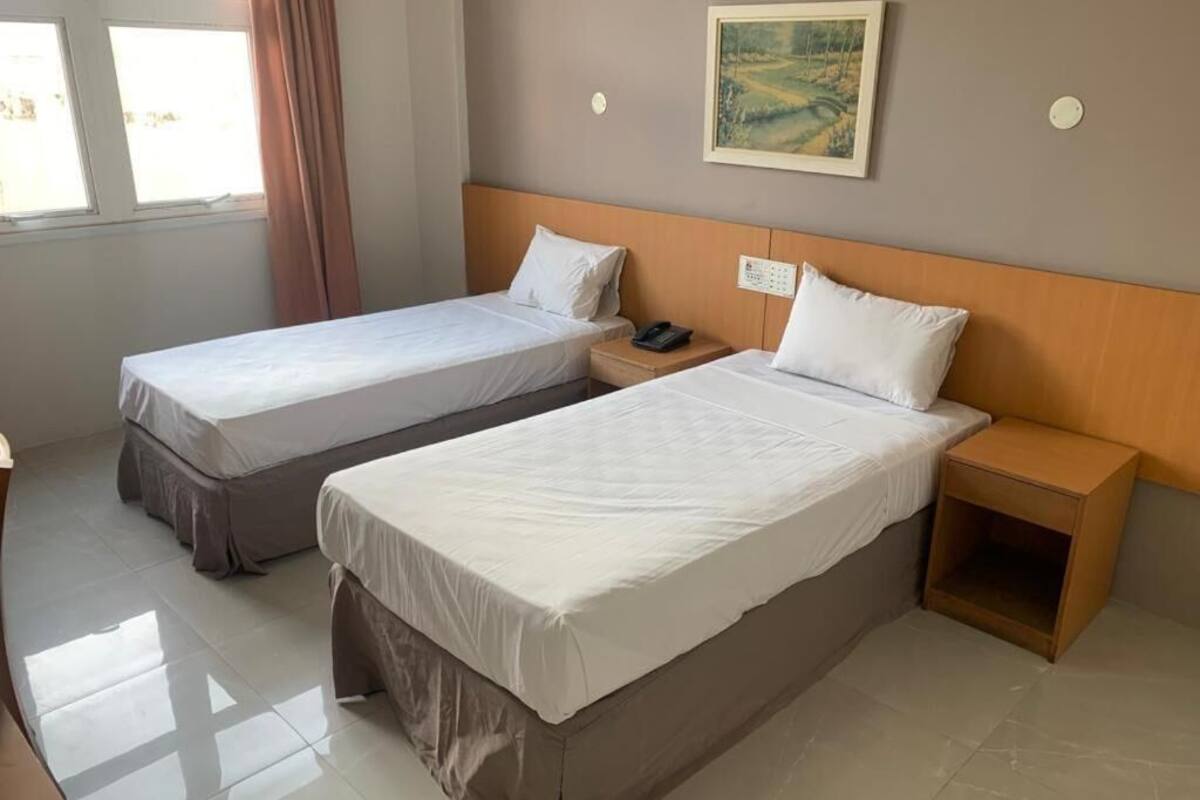 Hotelkamer met twee enkele bedden, een houten hoofdbord, een nachtkastje met telefoon en een schilderij aan de muur.