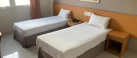 Habitación de hotel con dos camas individuales, cabecera de madera, mesita de noche con teléfono y un cuadro en la pared.