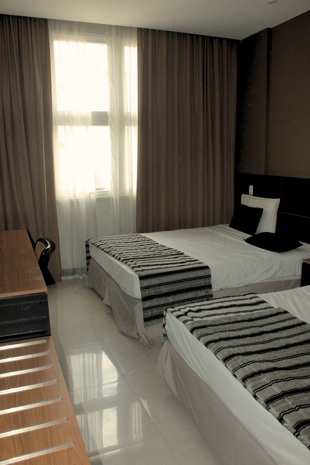 Habitación de hotel con dos camas, un escritorio y un ventanal grande con cortinas.