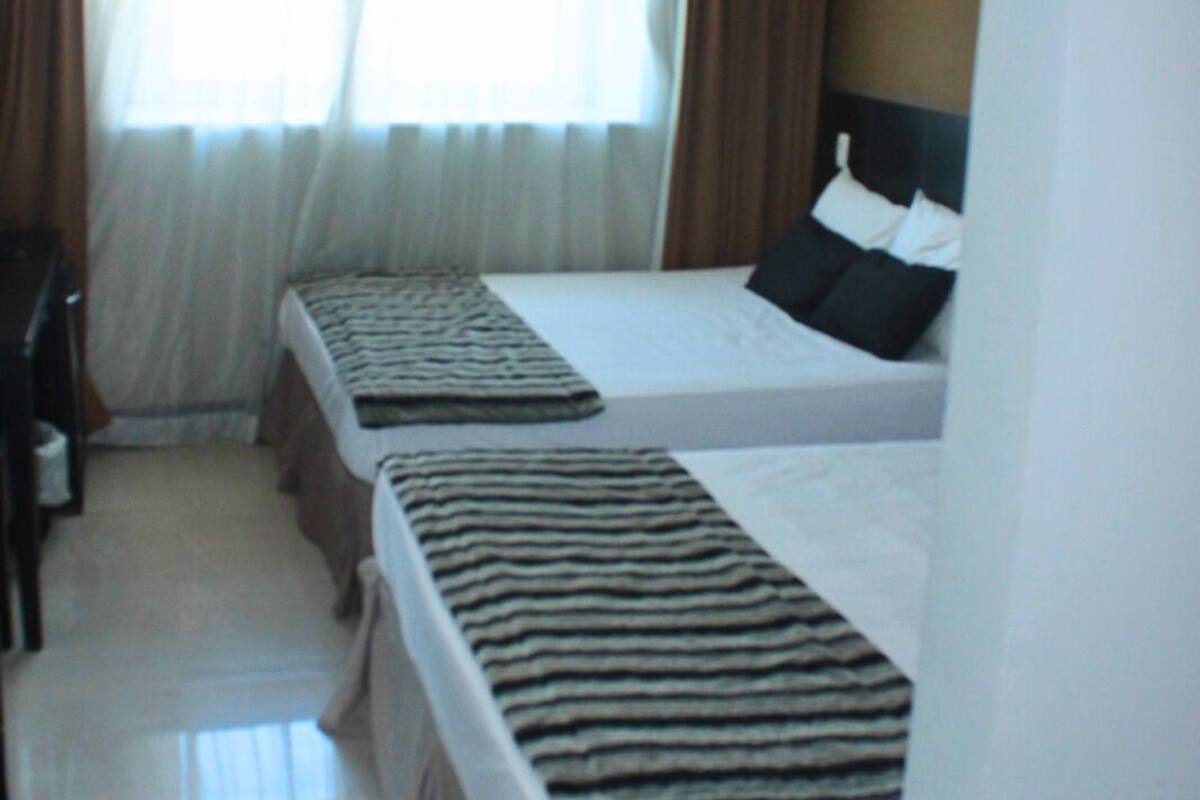 Een hotelkamer met twee bedden, een bureau en een raam met gordijnen.
