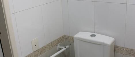 A small, white bathroom with a toilet, a handrail, and a towel on the seat.