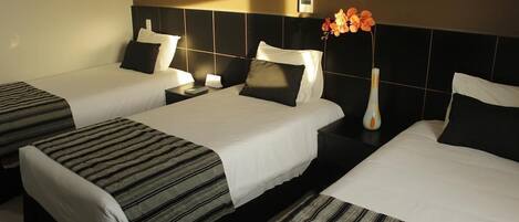 Habitación de hotel con dos camas individuales, una mesita de noche con lámpara y un florero con flores.