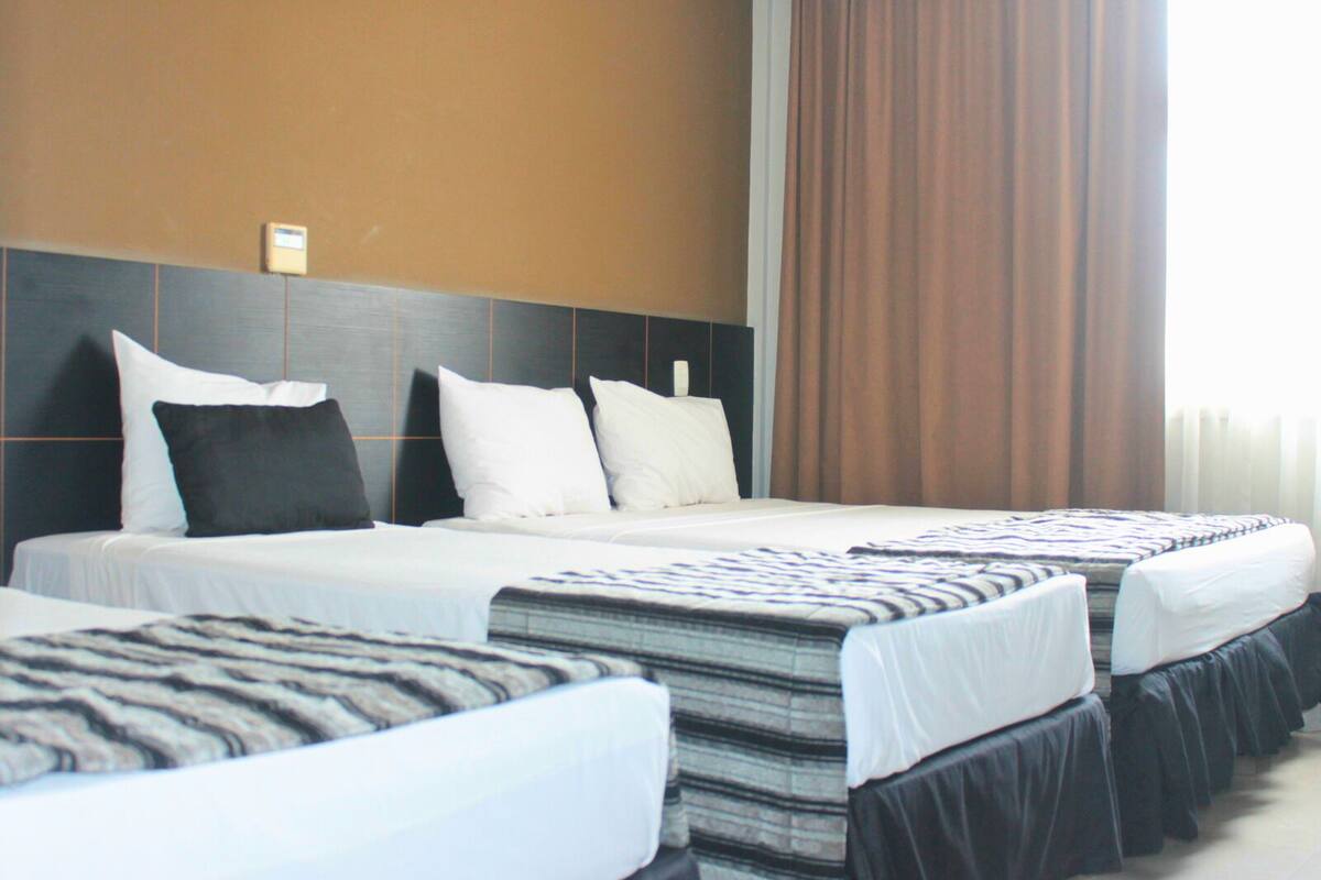 Een hotelkamer met twee bedden, een hoofdeinde en een groot raam met gordijnen.