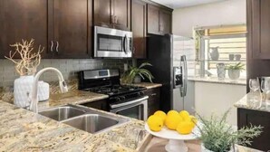 Una cocina con armarios de madera oscura, electrodomésticos de acero inoxidable, encimeras de granito y un lavamanos.