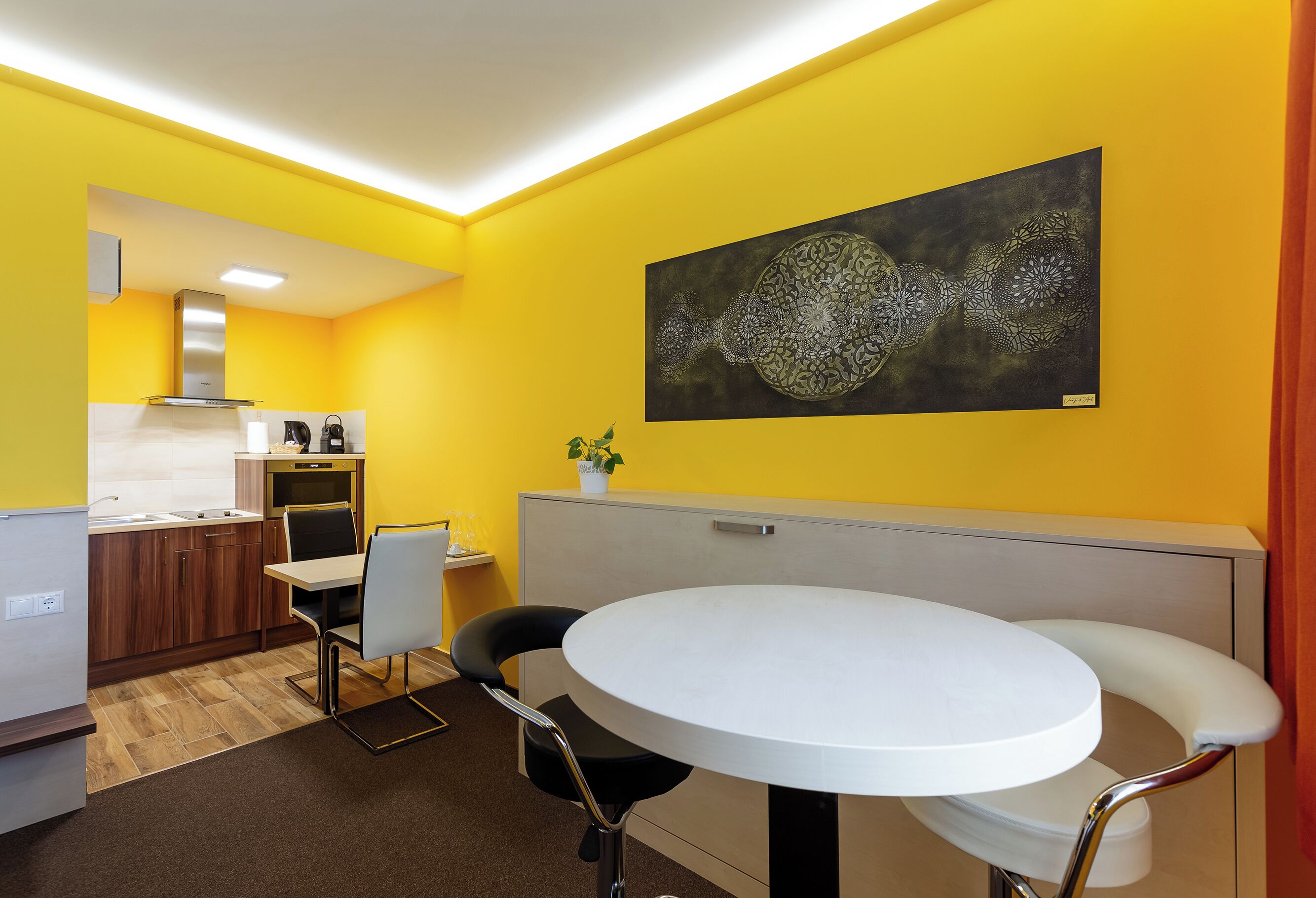 A modern kitchen with a dining area, a large abstract painting on the wall, and a bright yellow color scheme.