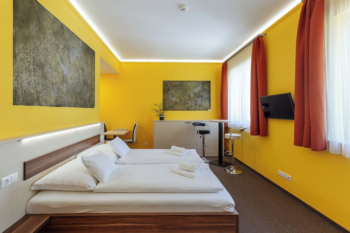 A hotel room with two beds, a desk, a chair, a TV, and artwork on the walls.