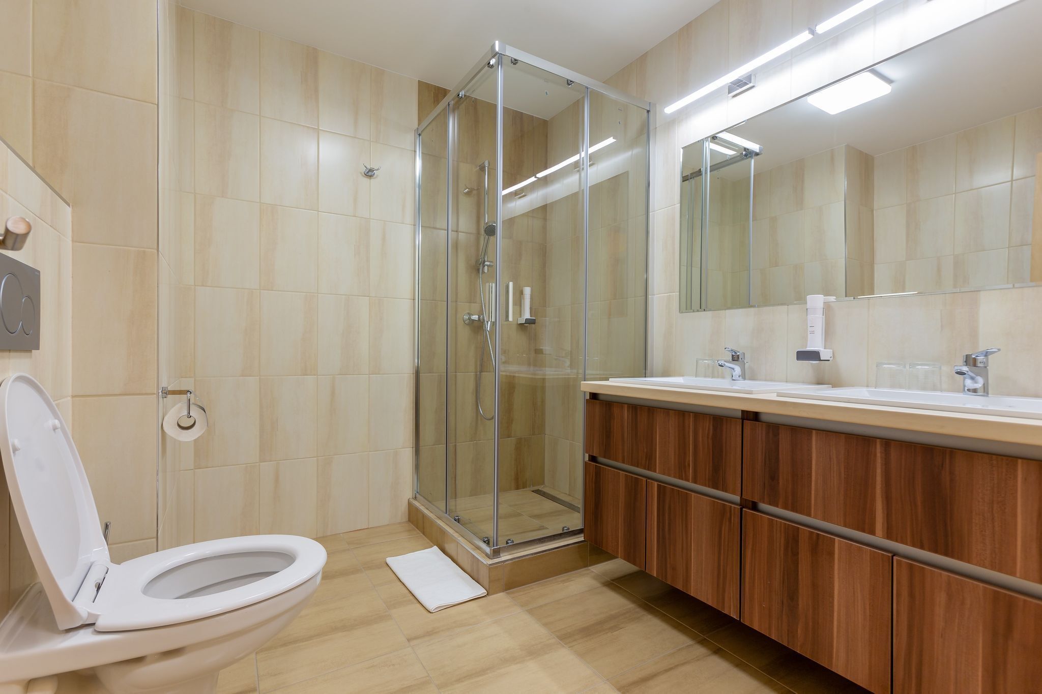 A modern bathroom with a glass-enclosed shower, a white toilet, and a wooden vanity with a mirror.
