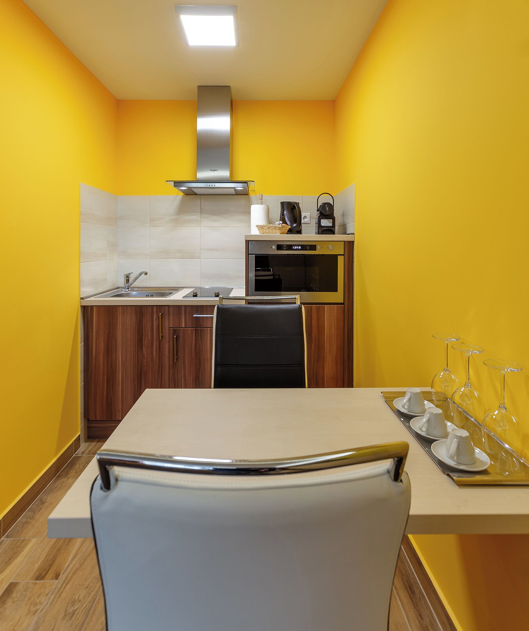 A compact kitchen with a sink, stove, and oven, a dining table with chairs, and a yellow wall.