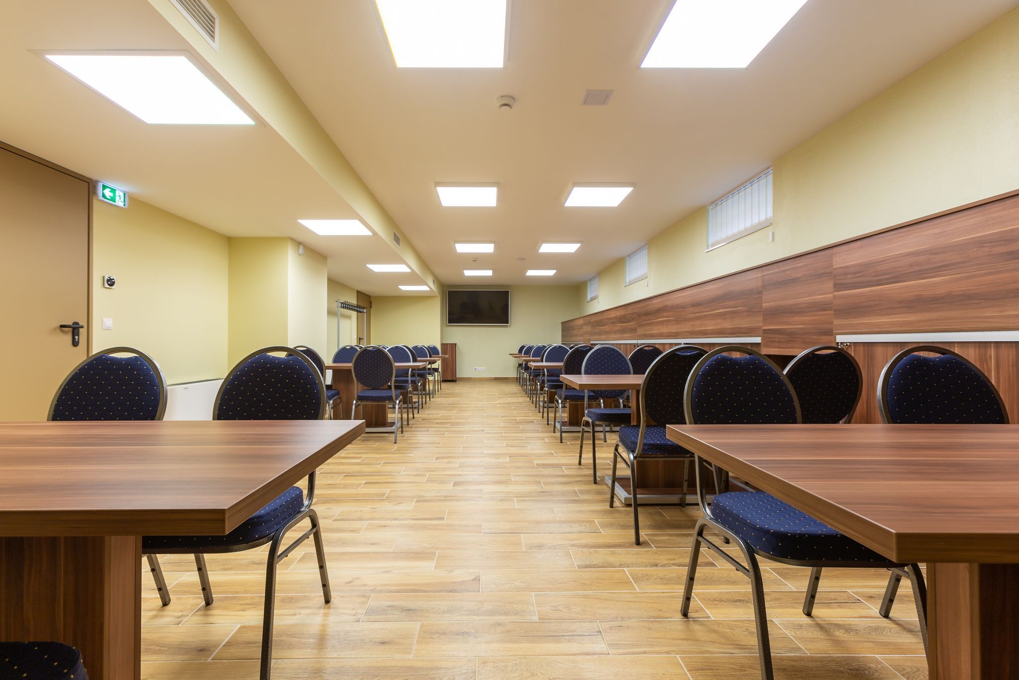 A conference room with multiple tables and chairs, a wooden panel wall, and a tiled floor.