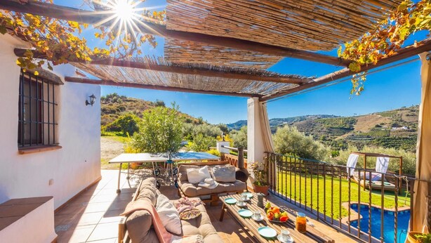 Patio esterno coperto con divano, tavolo da pranzo e sedie, affacciato su una piscina e dolci colline.