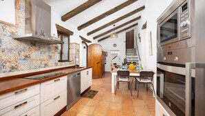 Una cucina con zoccolo piastrellato, travi in legno, forno a incasso e un'area pranzo con tavolo e sedie.