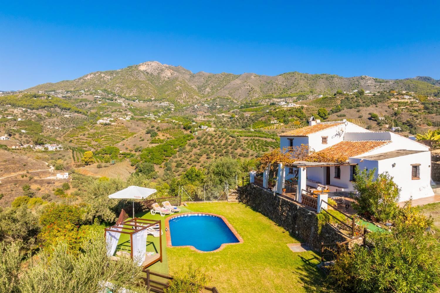 A white villa with a swimming pool, surrounded by lush greenery and hills in the background.