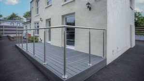A building with a white exterior, a metal staircase with a handrail, and a small outdoor area with a bench and potted plants.